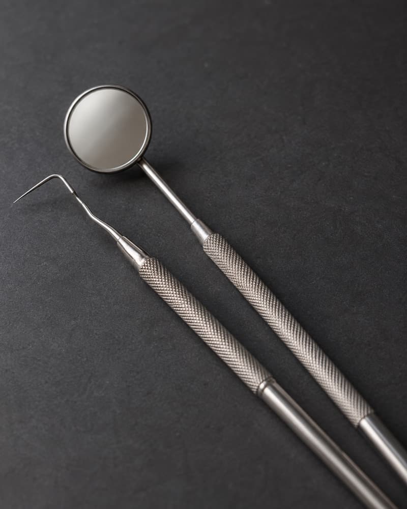 A dental mirror and explorer laid on a dark surface