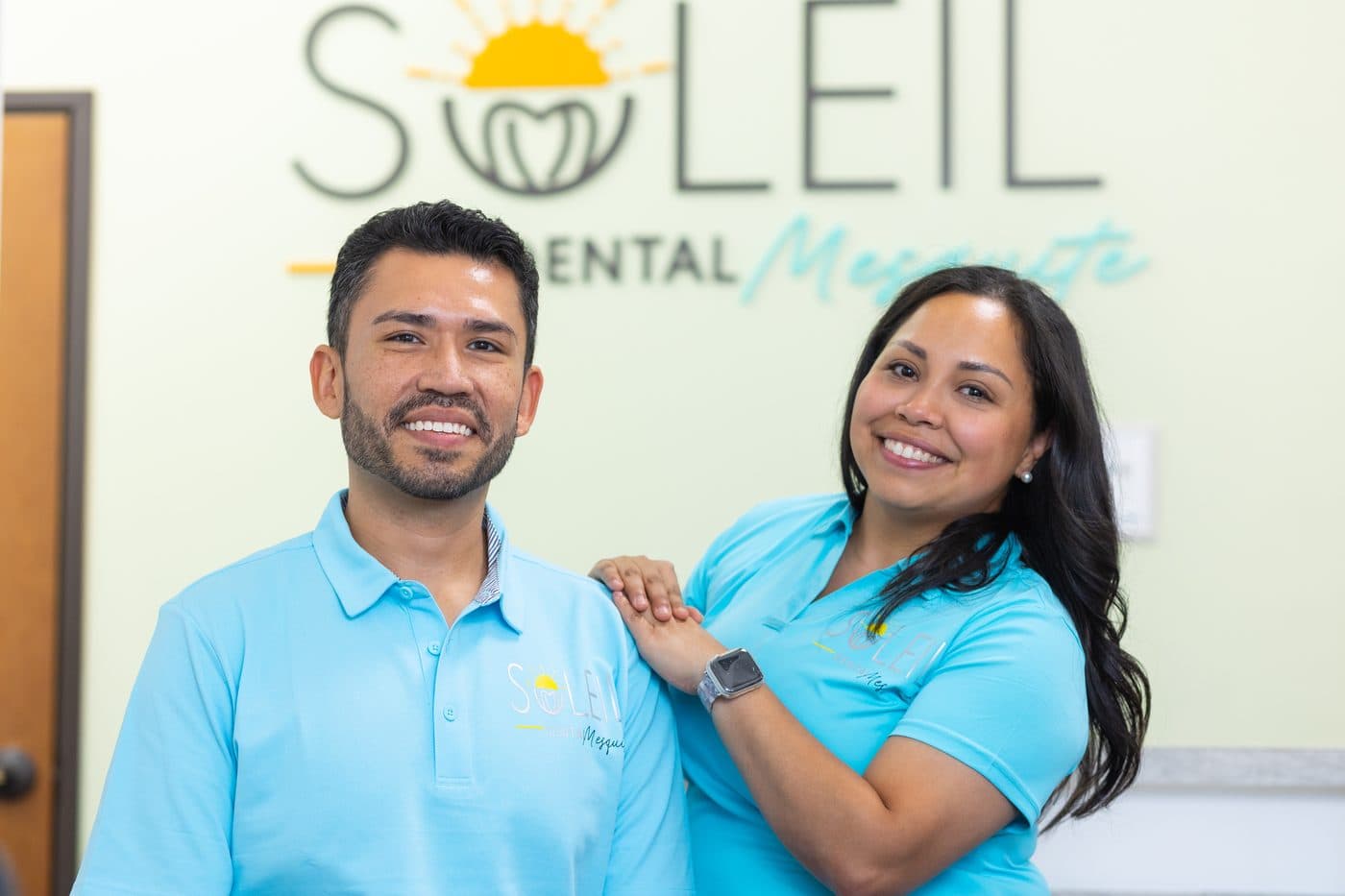 Dr. Diana Vazquez and Dr. Jose Aldana in front of the Soleil Dental Mesquite logo wall