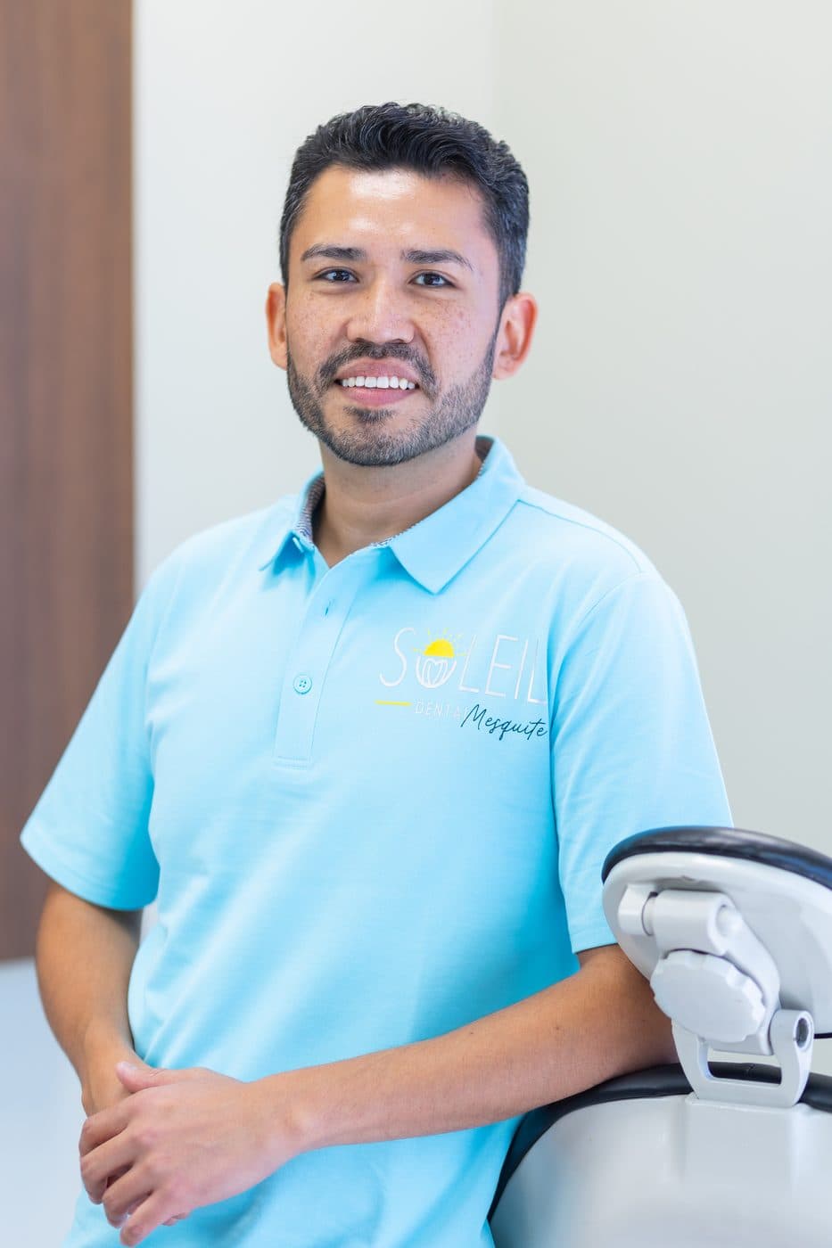 Dr. Jose Aldana in a teal Soleil Mesquite polo, standing beside a dental chair