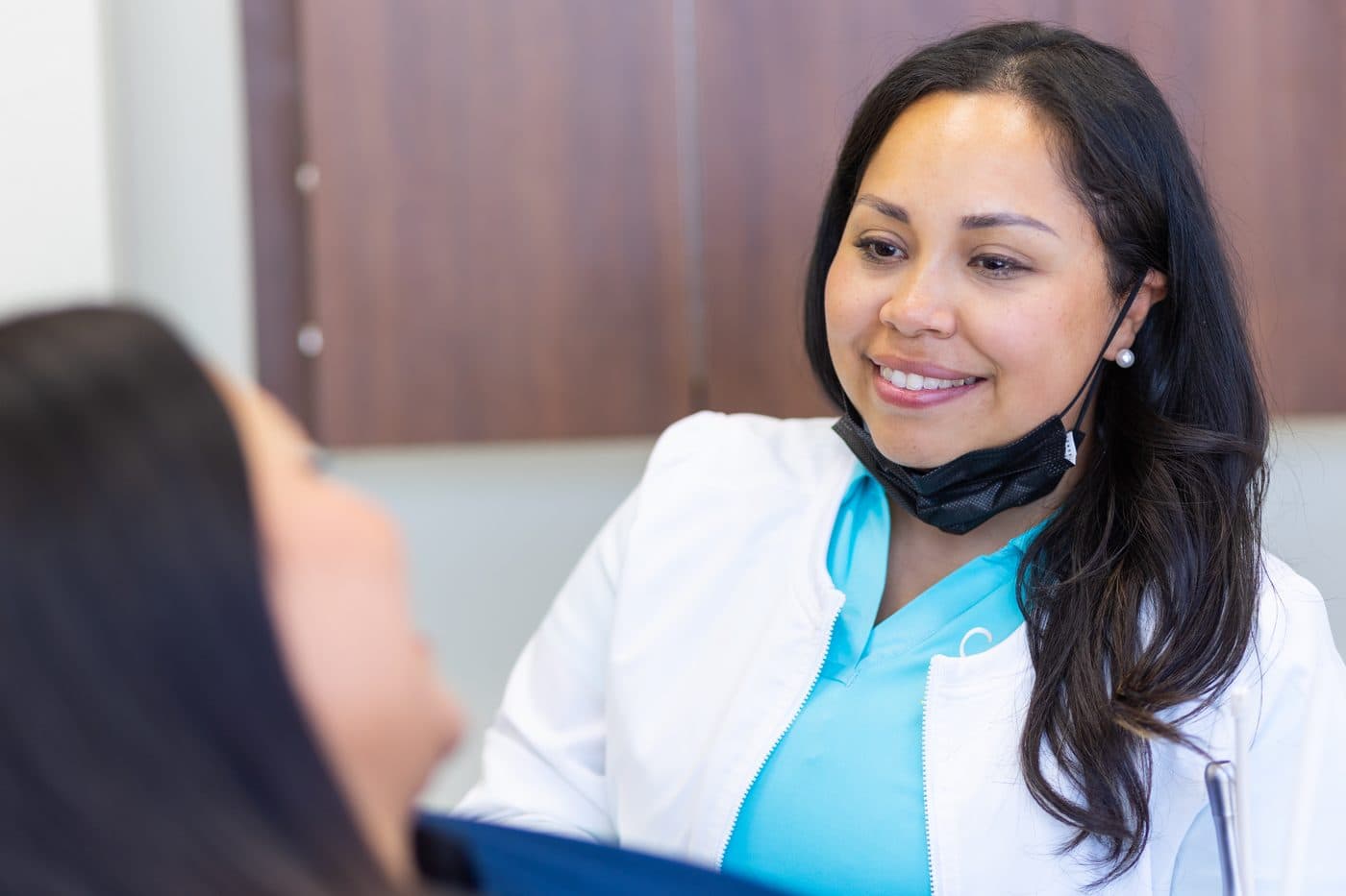 Dr. Diana Vazquez in a white coat, smiling as she talks with a patient in the chair