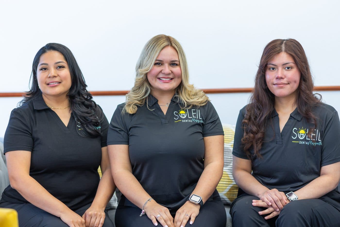 Three Soleil Dental Mesquite team members smiling on the waiting room sofa
